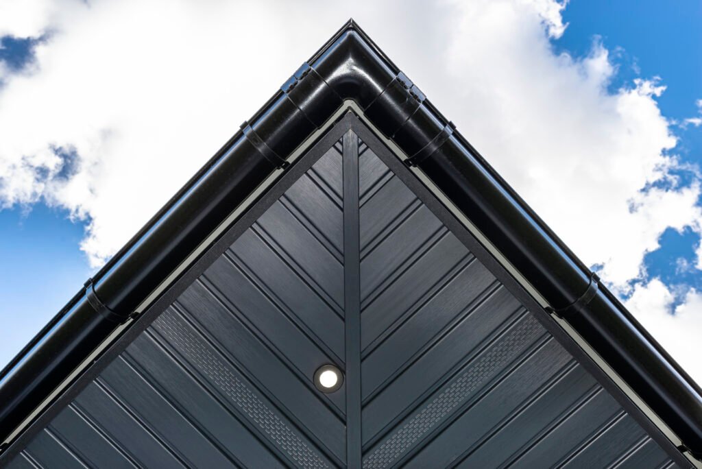 Une sous-face de toiture moderne en graphite à chevrons est fixée aux fermes, avec des lumières LED allumées et visibles.